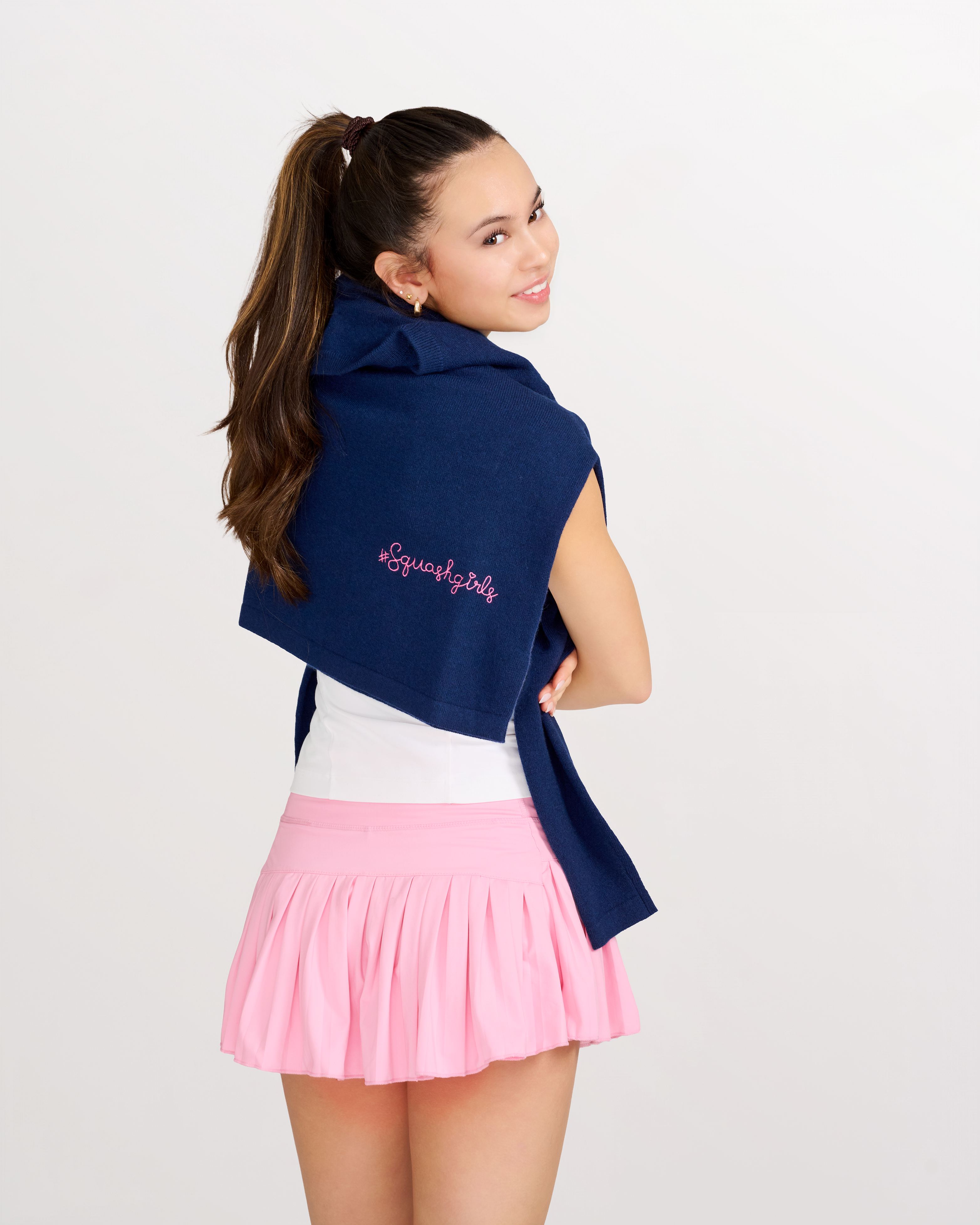 Woman wearing a navy cashmere sweater over her shoulders with pink text and a pink skirt on a white background.