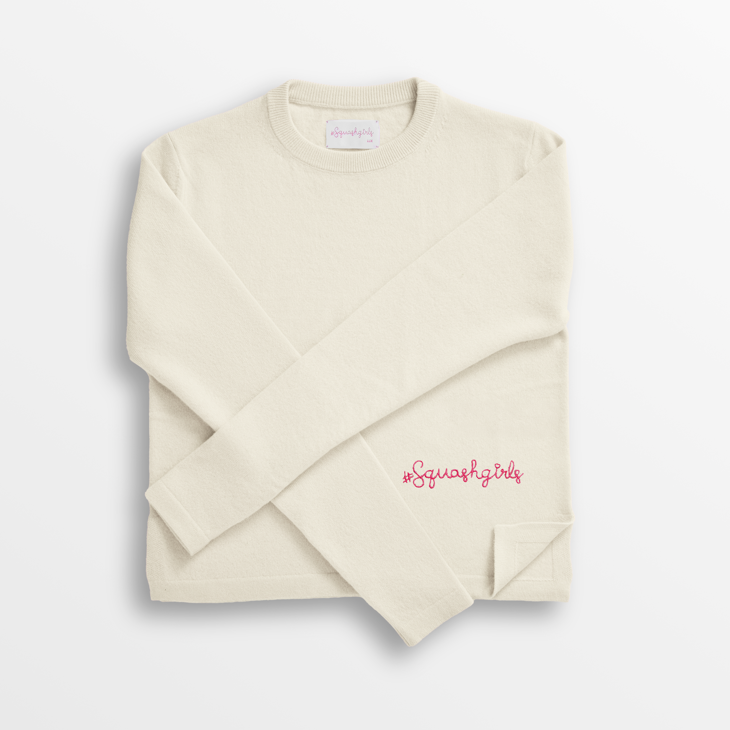 Folded beige cashmere sweater with 'Squash Girl' text on a white background