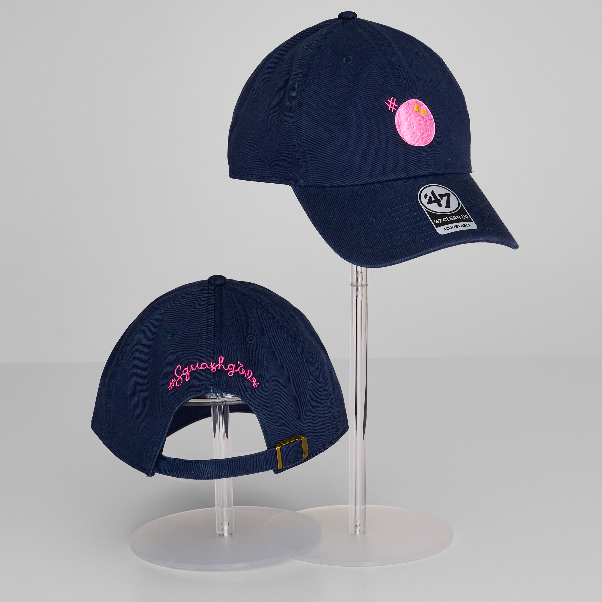 Two navy blue baseball caps with pink embroidery on a gray background
