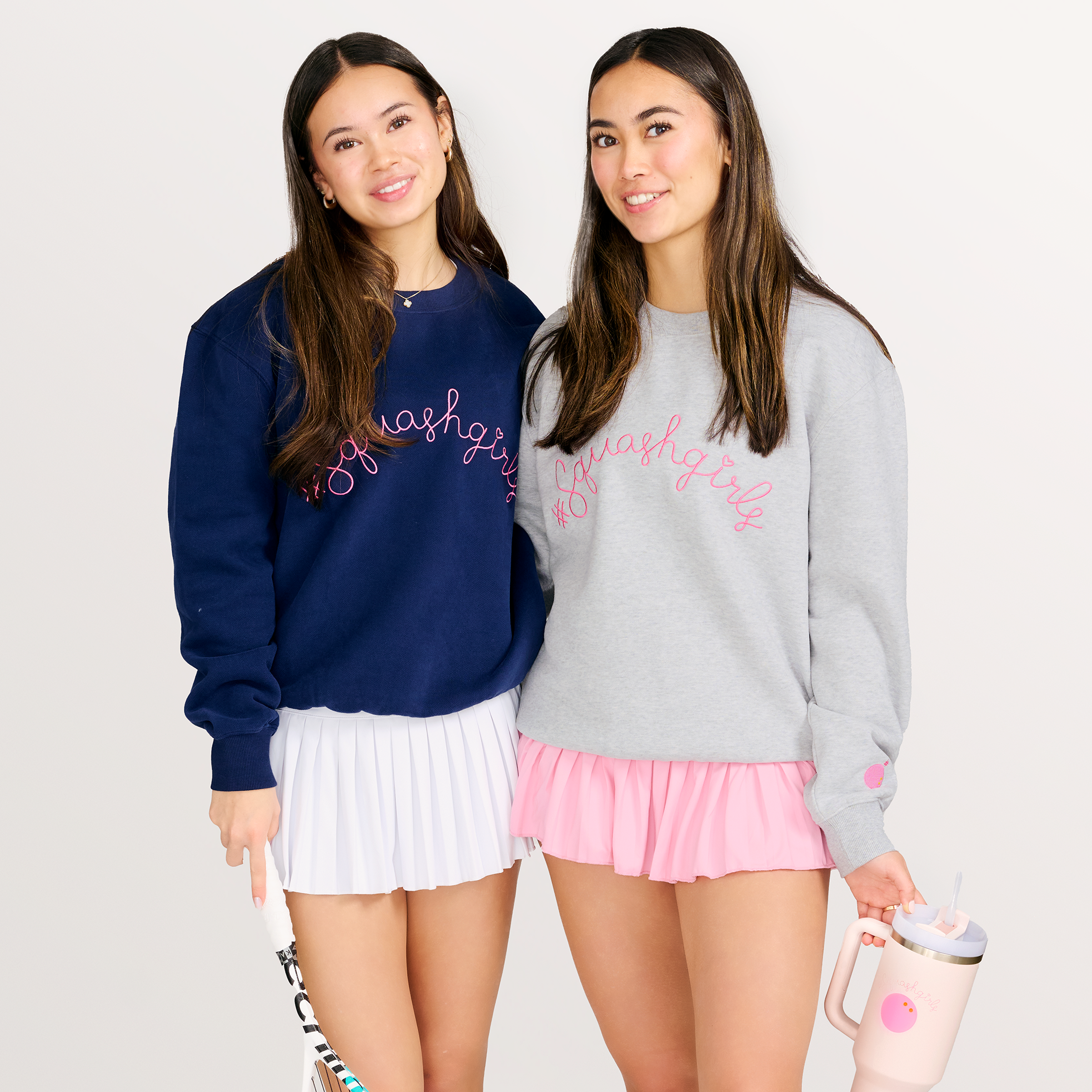 Two girls in matching outfits with squash equipment on a white background