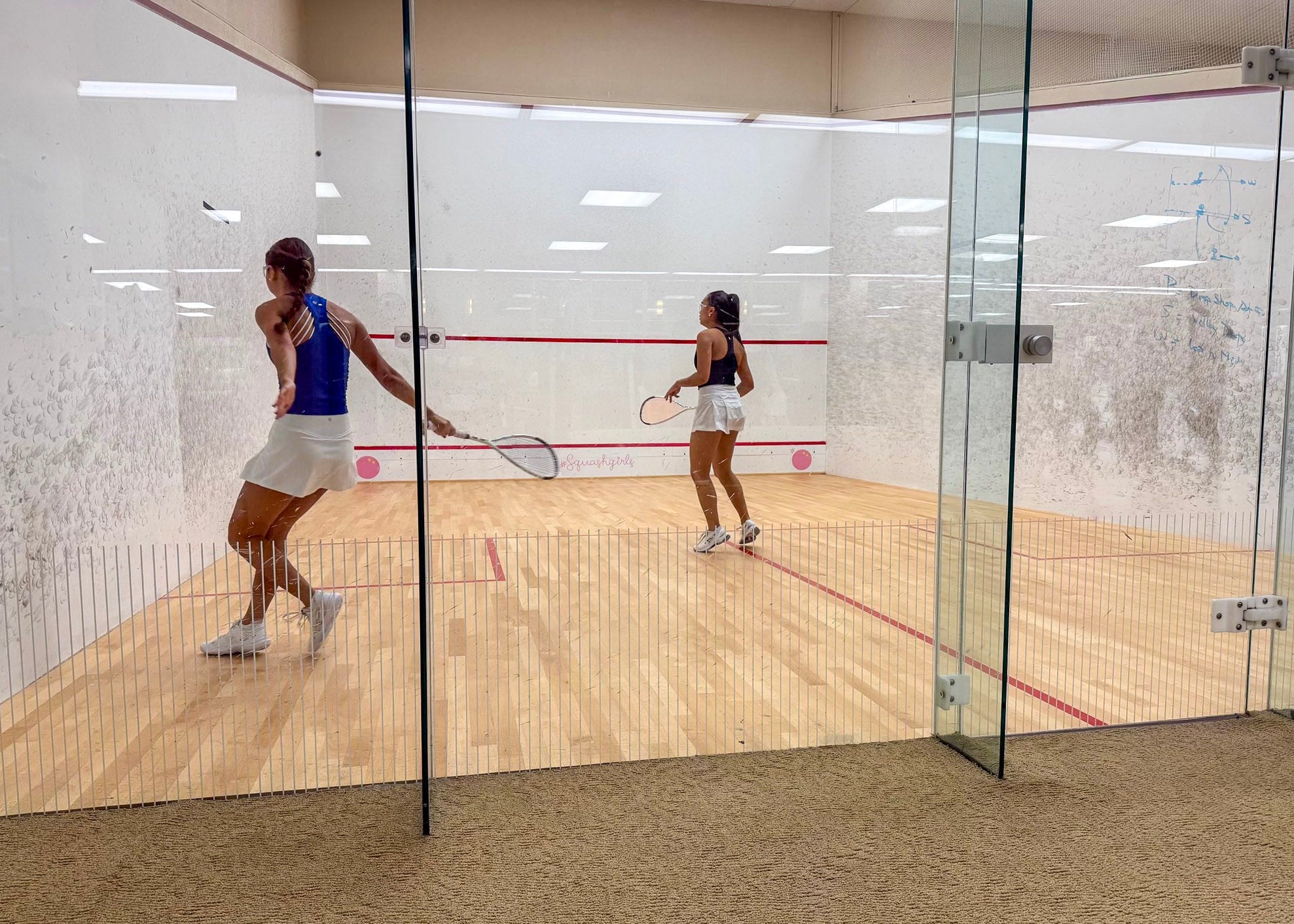 Two people playing squash in a glass-walled court.